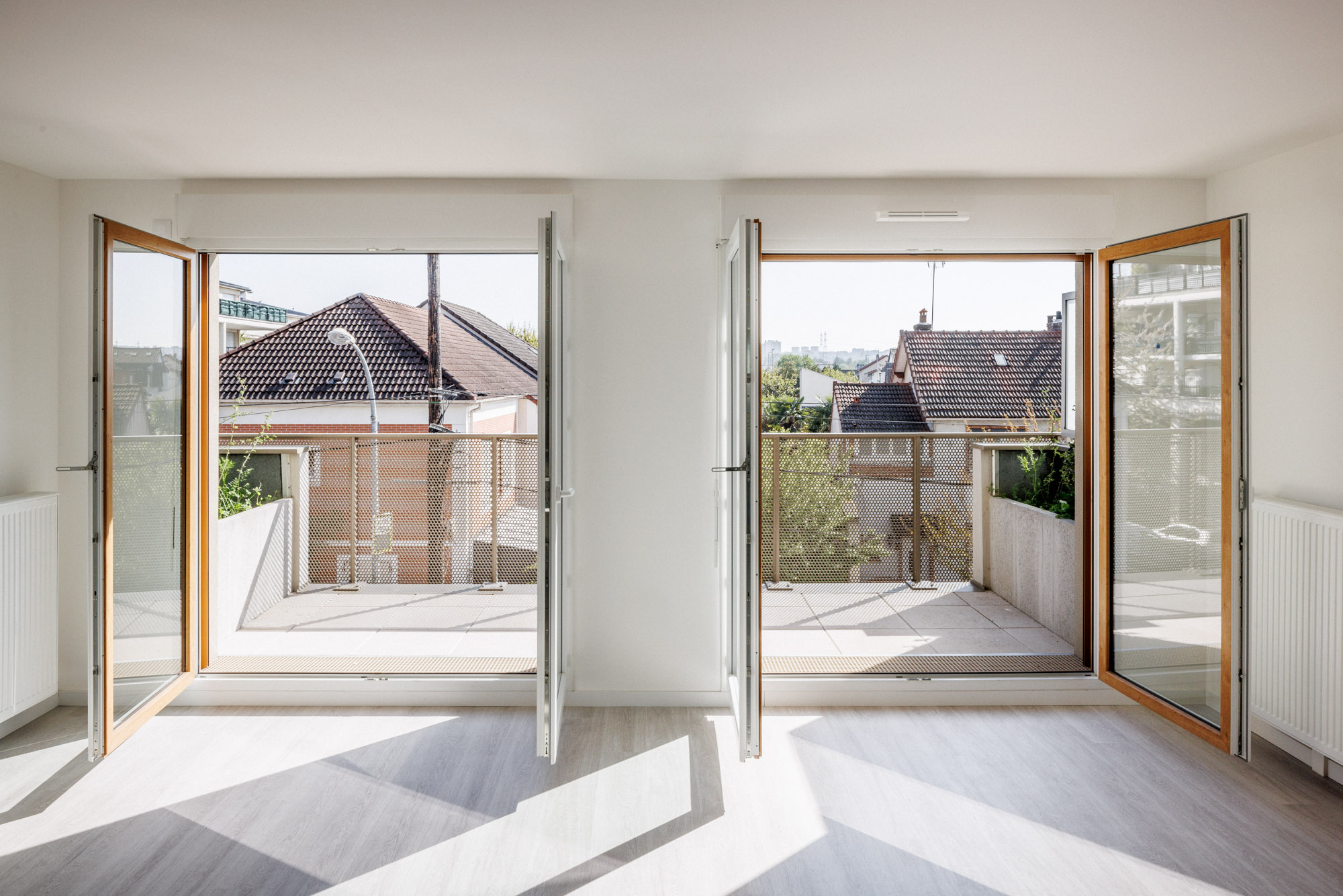 Séjour lumineux d'un logement de la résidence de 56 logements collectifs conçue par Cussac Architectes & Associés (CA+A) à Bondy (Seine-Saint-Denis), avec grandes baies vitrées ouvrant sur un balcon, favorisant la lumière naturelle et donnant sur les maisons avoisinantes.
